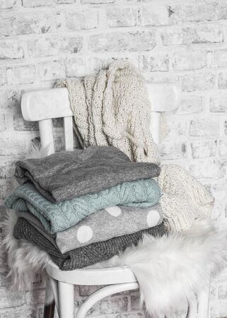 Stack of cozy winter autumn sweaters on an old white wooden chair in a light roomの写真素材