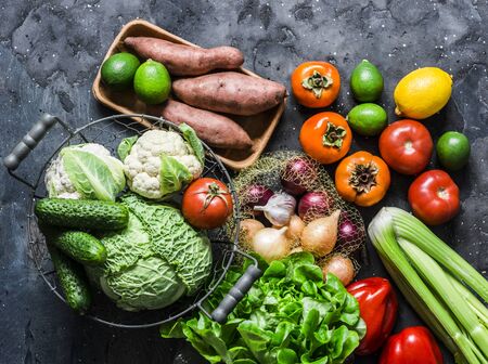 Fresh organic vegetables, fruits on a dark background, top view. Healthy diet food concept. Sweet potato, savoy cabbage, sweet peppers, celery, cucumbers, tomatoes, persimmon - delicious vegetarian foodの写真素材
