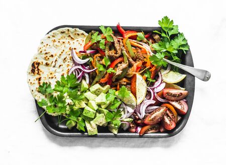 Spicy beef, vegetables, avocado, corn tortillas fajitas on a sheet pan on a light background, top...