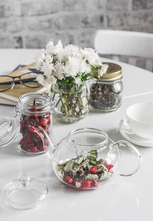 Kitchen table with herbal rosehip tea teapot, chrysanthemum bouquet, books. Cozy lazy home still lifeの写真素材