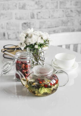 Currant, raspberry leaves, rose hips herbal tea in glass teapot on kitchen table. Rising immunity. Home cozy still lifeの写真素材