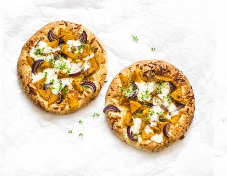 Cheesy autumn veggie flatbread. Pumpkin, sweet potato, red onion, mozzarella pizza on light background, top viewの写真素材