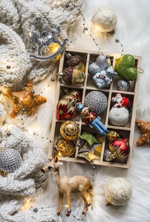 Knitted plaid, box of christmas toys, light garland on fluffy carpet, top view. Christmas backgroundの写真素材