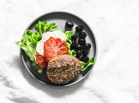 Delicious snack - multigrain bun, homemade cheese, tomato, green salad sandwich on a light background, top viewの写真素材
