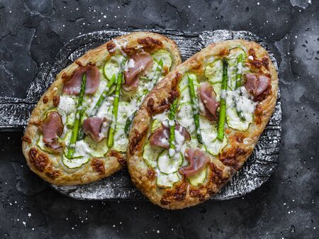 Puff pastry ham, zucchini, asparagus, mozzarella cheese pizza no wooden rustic chopping board on dark background, top viewの写真素材