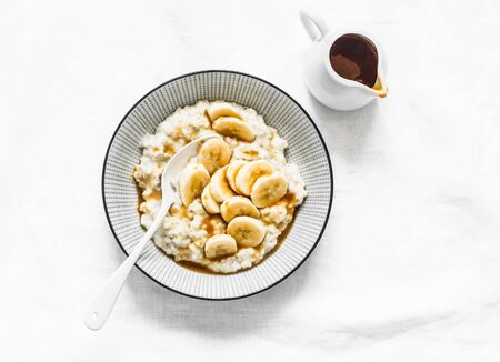 Toffee sauce banana oatmeal porridge - delicious healthy breakfast on white backgroundの写真素材