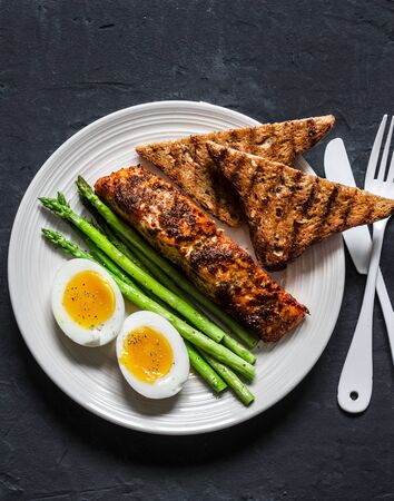 Healthy diet lunch - baked salmon, boiled soft eggs, asparagus and wholegrain bread on a dark background, top viewの写真素材