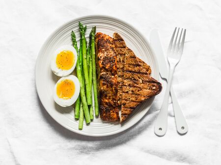 Healthy diet lunch - baked salmon, boiled soft eggs, asparagus and wholegrain bread on a light background, top viewの写真素材