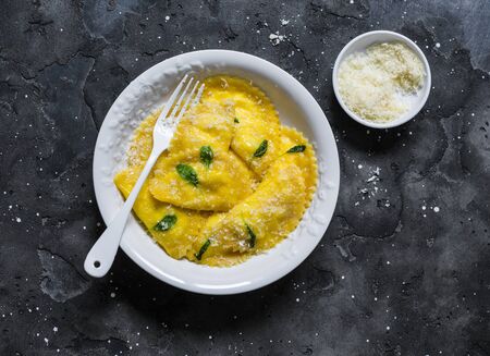 Pumpkin dough cheese ravioli with sage butter on a dark background, top view. Comfort autumn winter food in mediterranean styleの写真素材