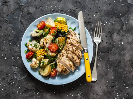 Chicken breast baked with potatoes, cauliflower, corn, eggplant, zucchini, cherry tomatoes on a dark background, top view. Healthy food diet conceptの写真素材