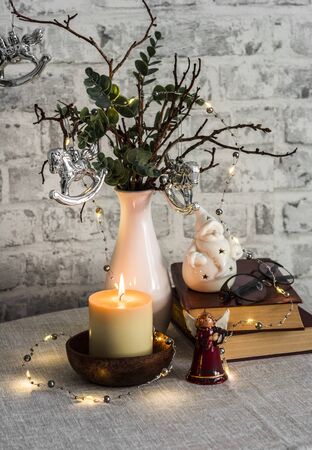 Christmas still life. Burning candle,stack of books, christmas tree, garland on the tableの写真素材