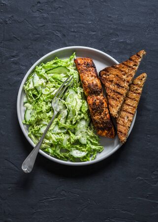 Crisp baked salmon and savoy cabbage, cucumber salad on dark background, top view. Healthy diet foodの写真素材
