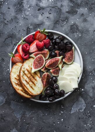 Snack appetizers tapas plate with cheese, figs, olives, berries on a dark background, top viewの写真素材