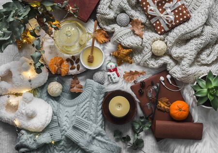 Christmas mood cozy home still life. Knitted plaid, sweater, books, green tea with honey, christmas toys, light garland, candle, soft slippers on the fluffy carpet, top view. Flat layの写真素材