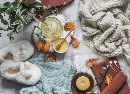 Cozy home still life - soft slippers, knitted sweater, plaid, green tea with honey, tangerines, dry leaves, books on a light background, top view. Autumn and winter a relaxing mood. Flat layの写真素材