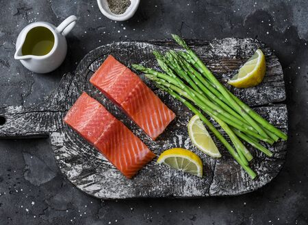 Ingredients for lunch - fresh raw organic salmon, green asparagus on a cutting board on a dark background, top viewの写真素材