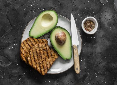 Fresh organic ripe avocado and whole grain grilled bread - delicious healthy breakfast, snack on dark background, top viewの写真素材