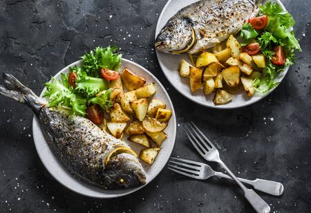 Delicious family lunch table - dorado fish baked with potatoes, lemon and sage on dark background, top viewの写真素材