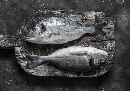 Fresh raw sea crucian dorado on rustic chopping board on dark background, top viewの写真素材