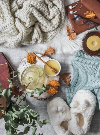 Cozy home still life - soft slippers, knitted sweater, plaid, green tea with honey, tangerines, dry leaves, books on a light background, top view. Autumn and winter a relaxing mood. Flat layの写真素材