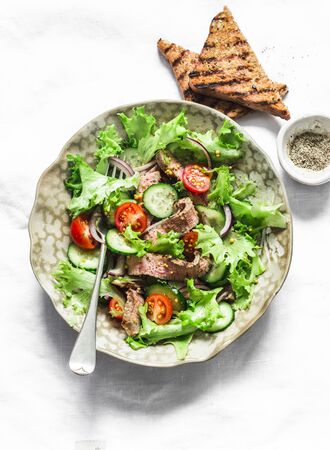 Warm salad with beef, cherry tomatoes, cucumbers, red onions, lettuce and lime mustard olive oil salad dressing on a light background, top viewの写真素材
