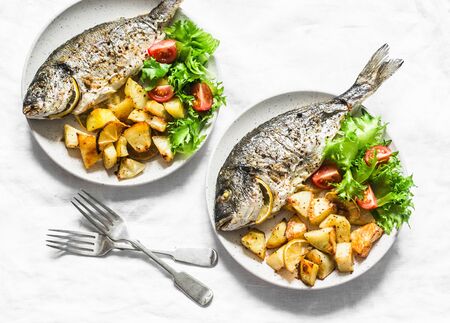Delicious lunch table - dorado fish baked with potatoes, lemon and sage on light background, top viewの写真素材