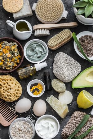 Face, body skin care homemade ingredients - cosmetic clay, brushes, homemade soap, coffee scrub, avocado, lemon, aloe, homemade oatmeal soap, calendula, chamomile dried flowers, natural yogurt on a dark background, top view. Beauty, healthy lifestyle concept. Flat layの写真素材