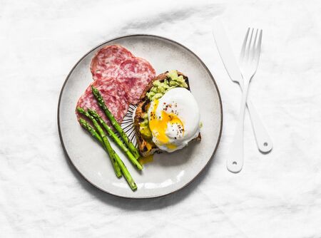 Delicious breakfast, brunch - poached egg on toast with avocado, salami and grilled asparagus on a light background, top viewの写真素材