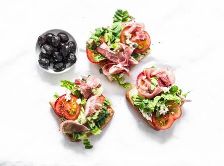Bruschetta with prosciutto, ciabatta bread, romano salad, tomatoes, cream cheese and sun dried olives on a light background, top viewの写真素材