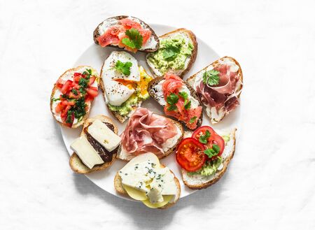 Variety of tapas sandwiches plate - sandwiches with prosciutto, avocado, salmon, egg, tomatoes, jamon, gorgonzola, brie, pear on a light background, top view. Delicious snack, appetizers. Copy spaceの写真素材