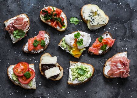 Variety of tapas sandwiches with prosciutto, avocado, salmon, egg, tomatoes, jamon, gorgonzola, brie, pear on a dark background, top view. Delicious snack, appetizersの写真素材