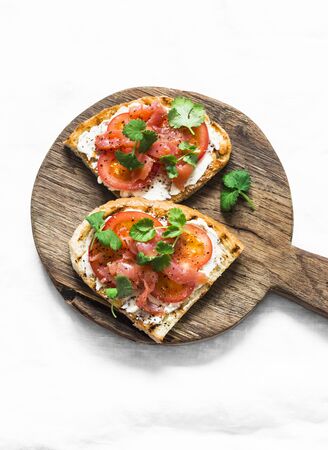 Smoked salmon, tomatoes, cream cheese, cilantro sandwich on a rustic cutting board on a light background, top viewの写真素材