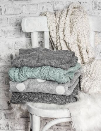 Stack of cozy winter women sweaters on an old white wooden chair in a light roomの写真素材