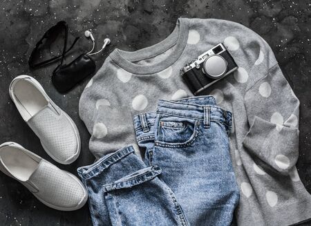Women's spring clothes for walking - mom's jeans, pullover, sneakers, sunglasses, headphones and camera on a dark background, top view. Fashion conceptの写真素材