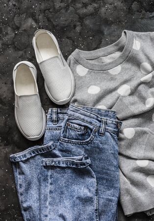 Women's spring clothes for walking - mom's jeans, pullover, sneakers  on a dark background, top view. Fashion conceptの写真素材