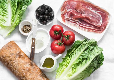 Ingredients for bruschetta - prosciutto, ciabatta bread, romano salad, olives, tomatoes, cream cheese on a light background, top view. Flat layの写真素材