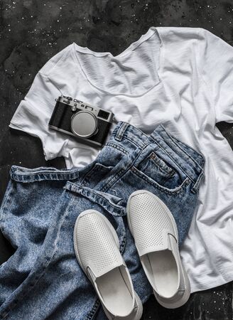 Simple women's look - white t-shirt, mom's jeans, white sneakers and a vintage camera on a dark background, top view. Fashion concept, flat layの写真素材