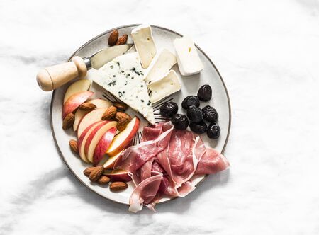 Appetizer plate - prosciutto, gorgonzola, brie cheese, olives, apples, nuts almonds on a light background, top viewの写真素材
