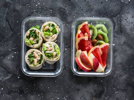 Healthy diet food lunch box - fruit and chicken, beans, green salad pita bread on a dark background, top view. Sweet b savory lunch boxの写真素材