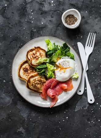 Healthy brunch - poached egg, smoked salmon, romaine salad and savory pancakes on a dark background, top viewの写真素材