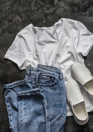 Simple women's look - white t-shirt, mom's jeans, white sneakers on a dark background, top view. Fashion concept, flat lay. Clothes for walkingの写真素材
