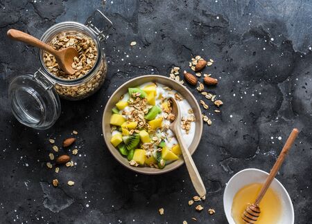 Greek natural yogurt with tropical fruits and granola on a dark background, top view. Natural yogurt with kiwi, mango and  peanut butter granolaの写真素材