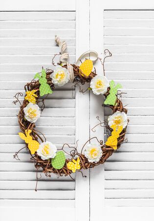 Homemade vine easter wreath with flowers and paper bunnies on a light background. Easter decoration for the house. Creativity conceptの写真素材