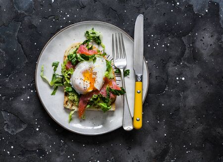 Sandwich with avocado, green salad, smoked salmon and poached egg on a dark background, top view. Delicious healthy nutritious breakfast, brunchの写真素材
