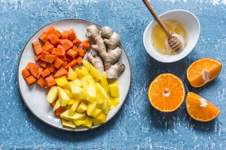 Ingredients for vitamin smoothies - fresh ripe mango, carrot, orange, honey, ginger on a blue background, top view. Detox healthy drinkの写真素材