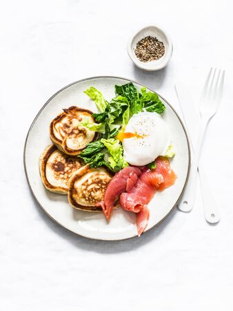 Delicious healthy brunch - poached egg, smoked salmon, green salad and savory pancakes on a light background, top viewの写真素材