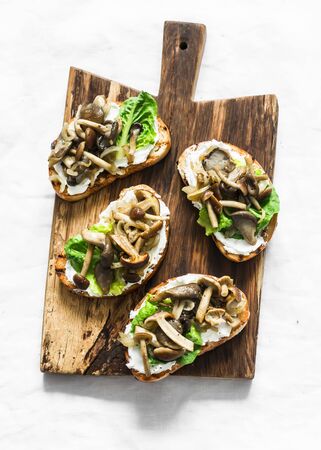 Mixed mushrooms cream cheese green salad on the grill bread sandwiches on a rustic cutting board on a light background, top viewの写真素材