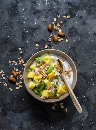 Greek yogurt with tropical fruits and granola on a dark background, top view. Natural yogurt with kiwi, mango and granola. Copy spaceの写真素材