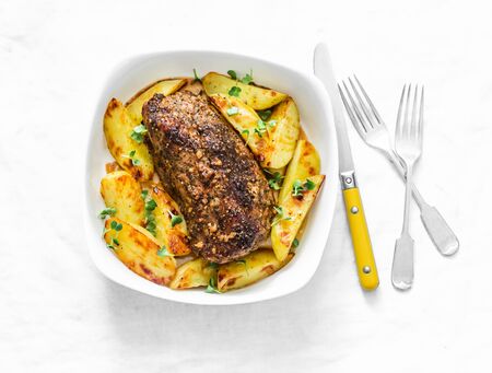 Baked pork fillet with potatoes and spices - delicious simple lunch on a light background, top viewの写真素材