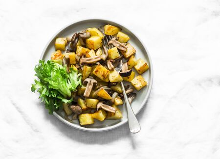 Fried potatoes with mushrooms and green salad - delicious simple vegetarian lunch on a light background, top viewの写真素材